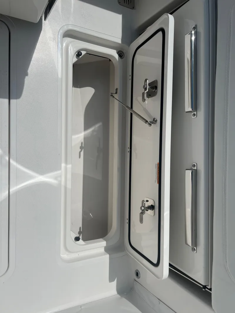 Slide: The Image of 2024 Pursuit DC 306 Dual Console storage compartment with open hatch and secure latches. - 12