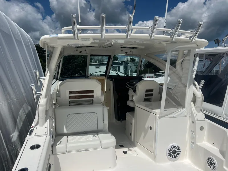 Slide: The Image of 2024 Pursuit DC 306 Dual Console boat interior with seating and rod holders under a cloudy sky. - 17