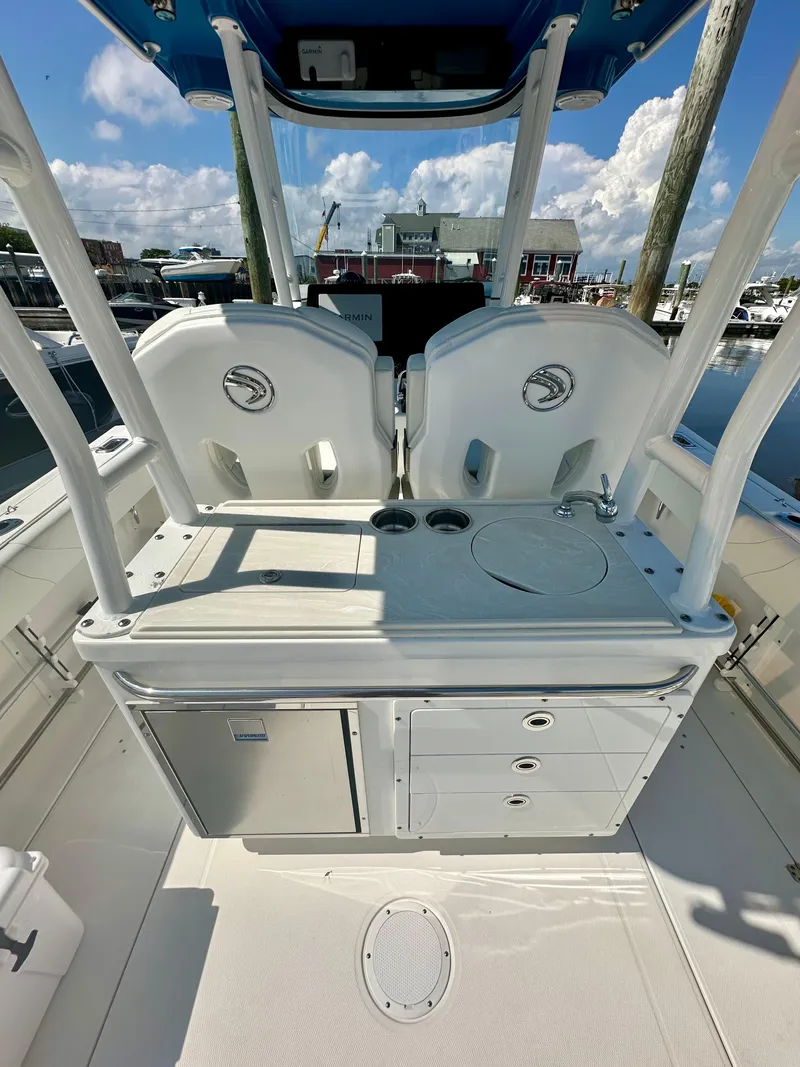 Slide: The Image of 2019 Edgewater 280CC boat interior with seating and storage, docked under a sunny sky. - 19