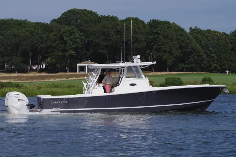 Slide: The Image of 2025 Regulator 37 boat cruising on a calm river with lush green trees in the background. - 2