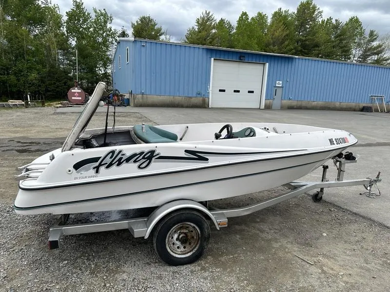 Slide: The Image of 1995 Four Winns Fling boat on trailer, parked outdoors near a blue building. - 5