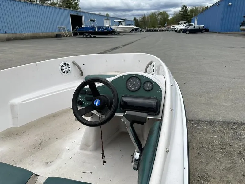 Slide: The Image of 1995 Four Winns Fling boat interior with steering wheel and dashboard in a marina setting. - 6