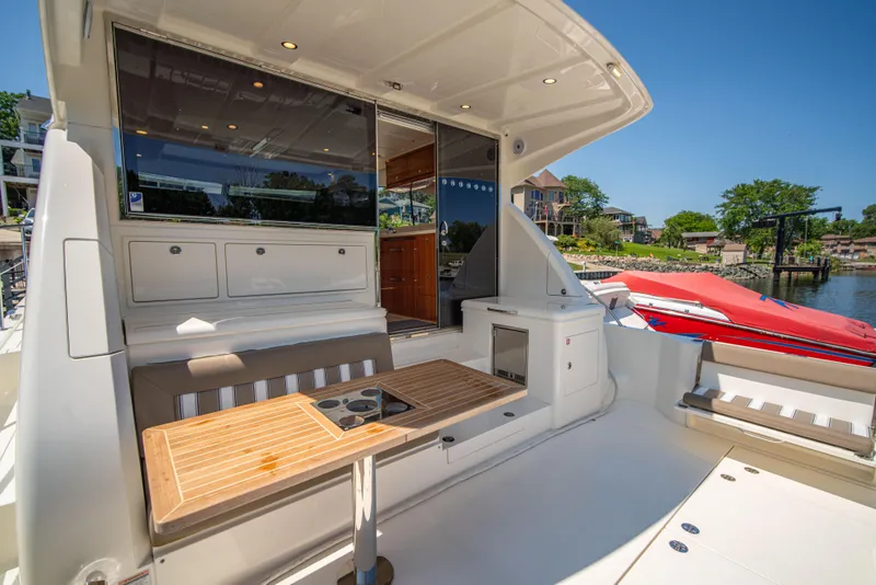 Slide: The Image of 2020 Riviera 525 SUV yacht with outdoor seating and table, docked by a scenic waterfront. - 15