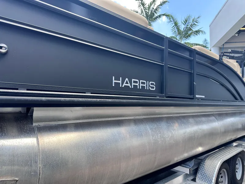 Slide: The Image of 2023 Harris Cruiser 230 pontoon boat, sleek black exterior, parked on a trailer. - 22