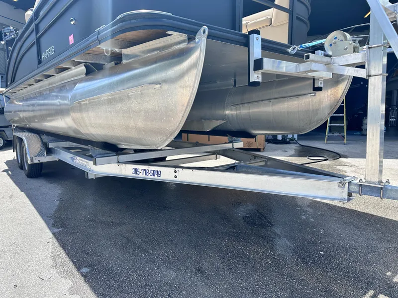 Slide: The Image of 2023 Harris Cruiser 230 pontoon boat on a trailer in a sunny outdoor setting. - 24