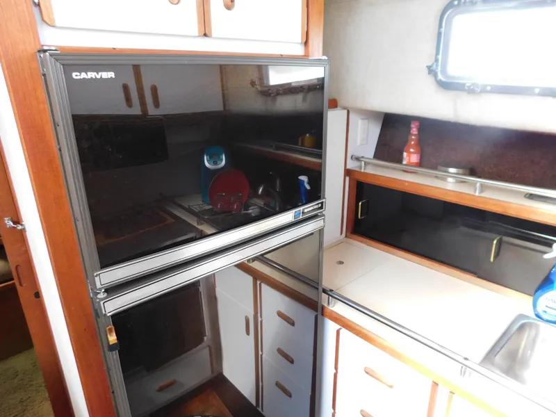Slide: The Image of 1985 Carver 3607 Aft Cabin kitchen with black fridge, wooden cabinets, and sink. - 17