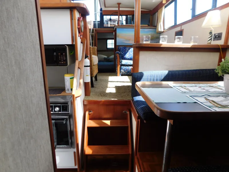 Slide: The Image of 1985 Carver 3607 Aft Cabin interior with dining area, kitchen, and cozy seating. - 23