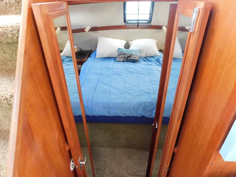 Slide: The Image of 1985 Carver 3607 Aft Cabin bedroom with blue bedding and wooden doors. - 25