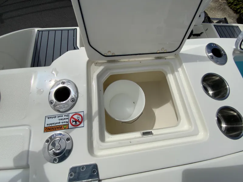 Slide: The Image of Cobia 265 Center Console Open 2025 boat storage compartment with cup holders and warning label. - 18