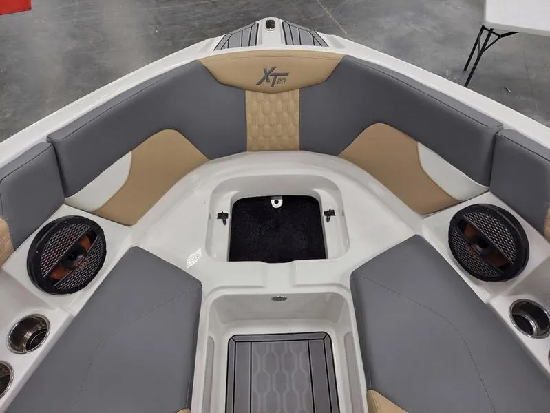 Slide: The Image of 2023 MasterCraft XT23 boat interior with gray and tan seating, featuring speakers and storage. - 25