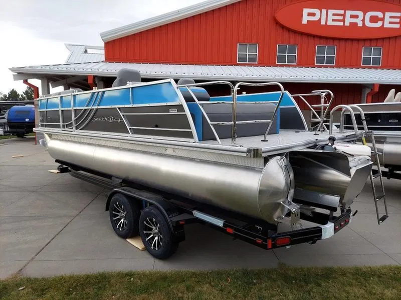 Slide: The Image of 2023 South Bay S224 UL 3.0 pontoon boat on trailer, parked outside red building. - 5