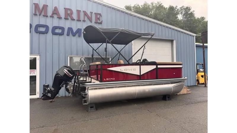 Slide: The Image of 2025 Lowe LS170 pontoon boat with canopy, parked outside a marine showroom. - 2