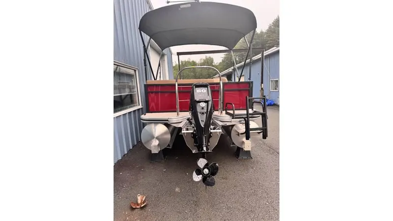 Slide: The Image of 2025 Lowe LS170 pontoon boat with canopy and outboard motor, parked near blue building. - 3