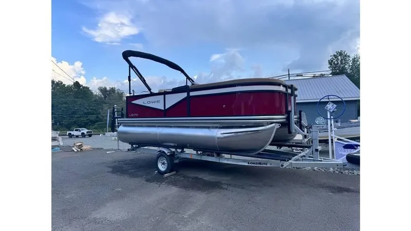 Slide: The Image of 2025 Lowe LS170 pontoon boat on trailer, parked outdoors under a blue sky. - 5