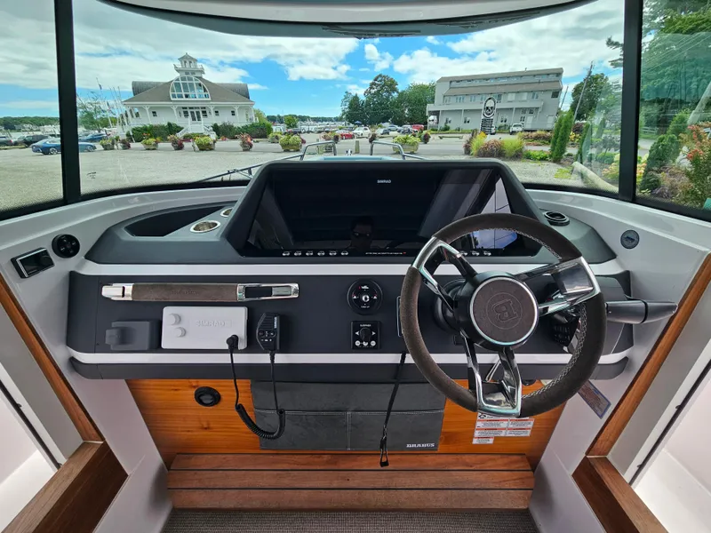 Slide: The Image of 2022 Axopar 28 boat dashboard with steering wheel and controls, marina view in background. - 23