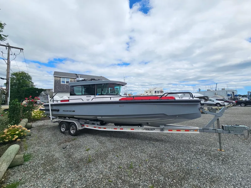 Slide: The Image of 2022 Axopar 28 boat on trailer in a gravel lot under cloudy sky. - 6