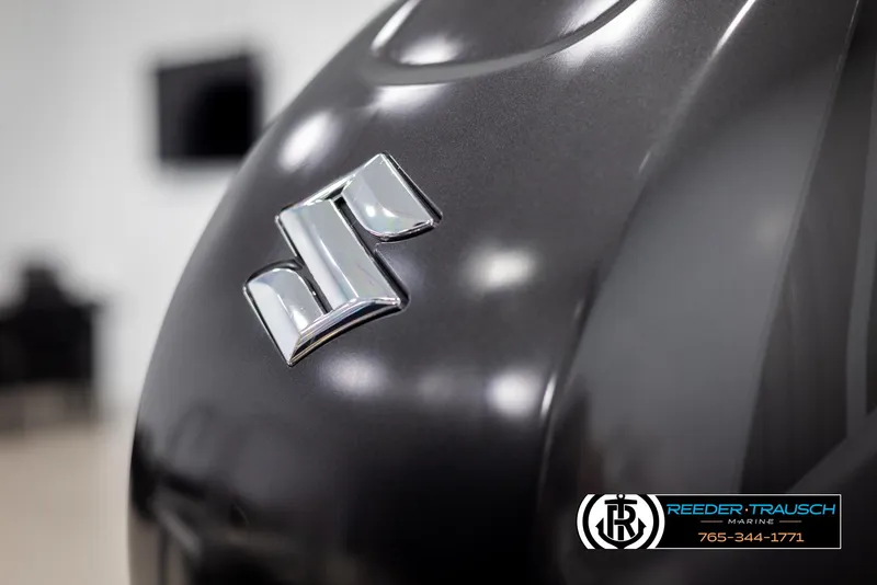 Slide: The Image of Close-up of a Suzuki logo on a sleek, dark surface, featuring Reeder-Trausch Marine branding. - 46