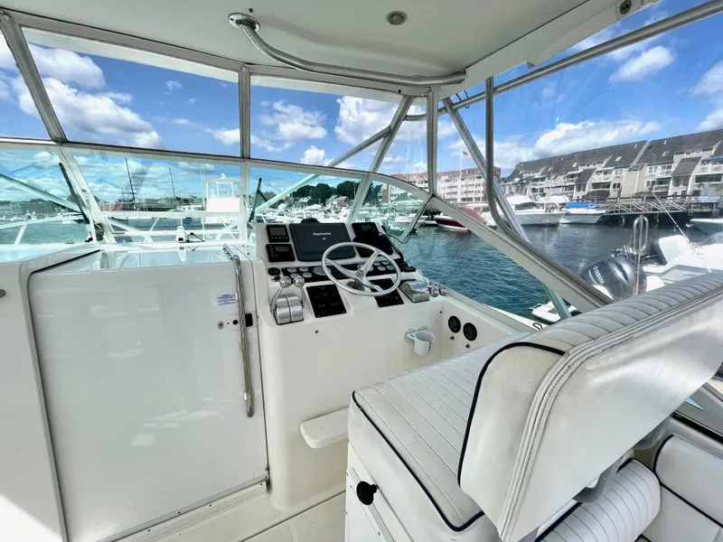 Slide: The Image of 1999 Cabo 31 Express boat helm with marina view, featuring steering wheel and controls. - 14
