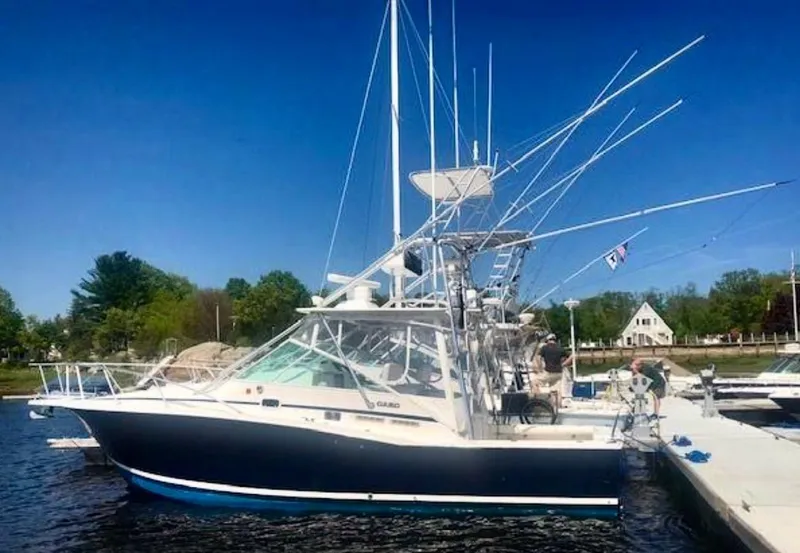 Slide: The Image of 1999 Cabo 31 Express boat docked, featuring fishing rods and a clear blue sky. - 24