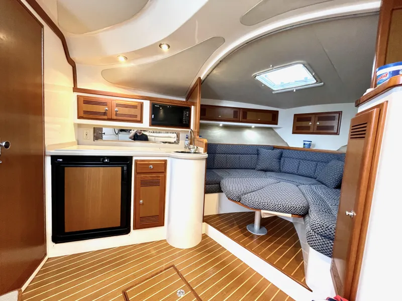 Slide: The Image of 1999 Cabo 31 Express cabin interior with seating, kitchenette, and wood accents. - 7