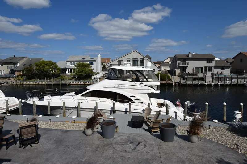 Slide: The Image of 2006 Sea Ray 58 Sedan Bridge yacht docked in a residential marina under a clear blue sky. - 2