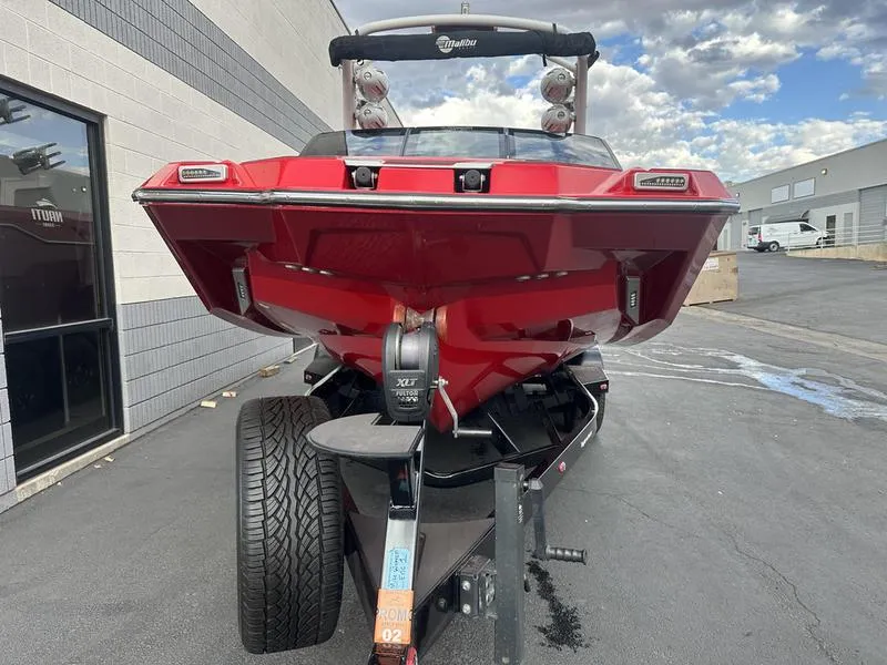 Slide: The Image of Red 2021 Malibu M240 boat on trailer, parked outdoors. - 9