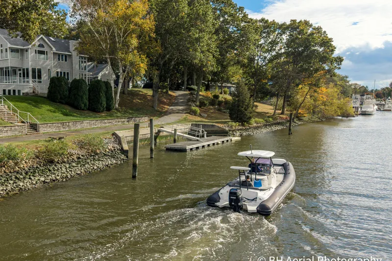 Slide: The Image of 2025 Grand Inflatables G850 boat cruising on a scenic river near waterfront homes. - 4