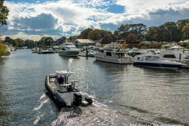 Slide: The Image of 2025 Grand Inflatables G850 boat cruising in a scenic marina with yachts and trees. - 5