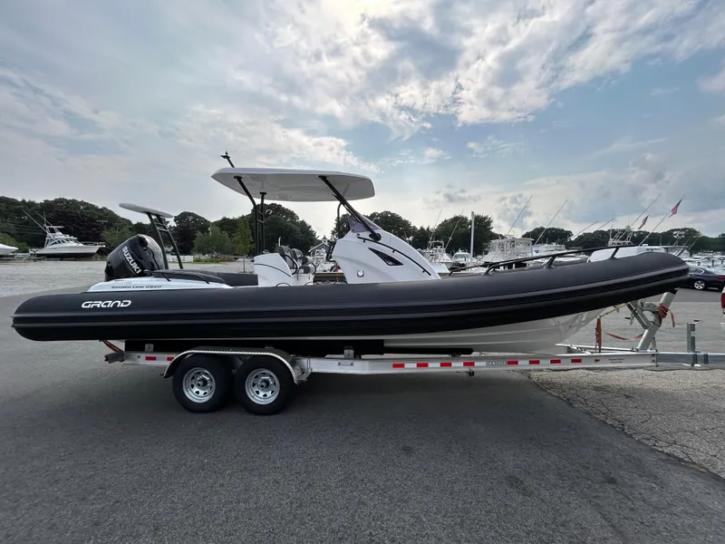 Slide: The Image of 2025 Grand Inflatables G850 boat on trailer, parked in marina under cloudy sky. - 8