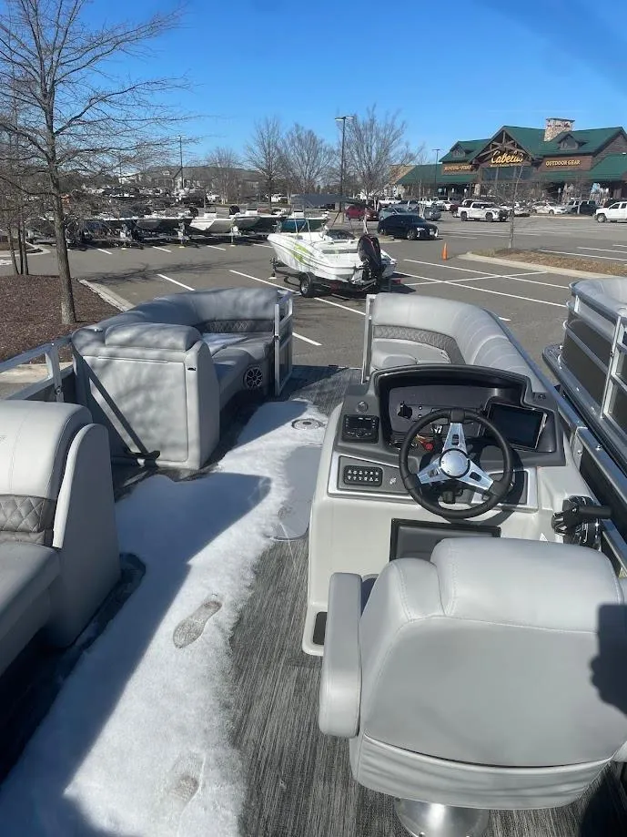 Slide: The Image of 2024 Ranger Reata 223C pontoon boat interior with steering console and seating, parked outdoors. - 2