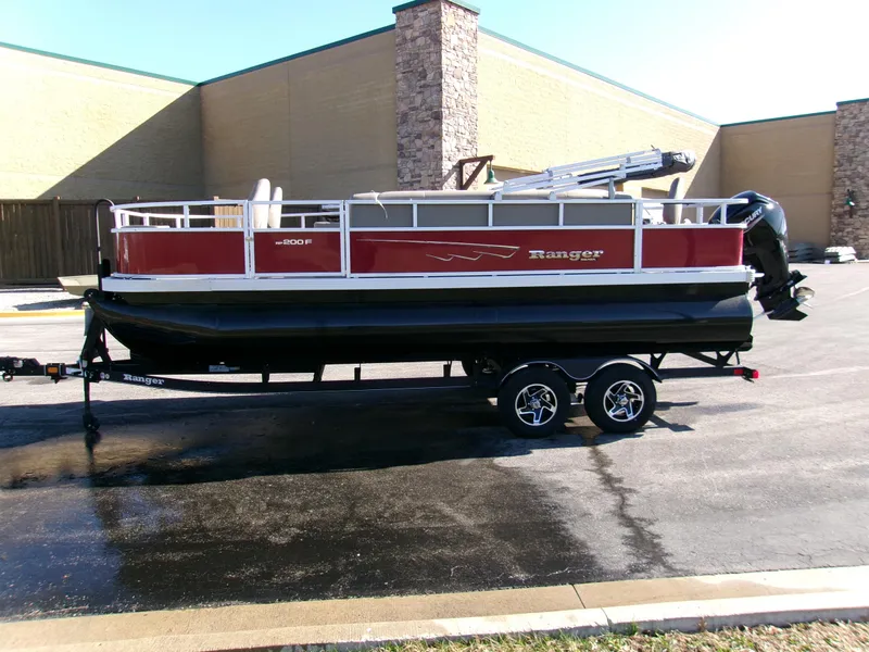 Slide: The Image of 2024 Ranger Reata 200F pontoon boat on trailer, parked outdoors. - 2