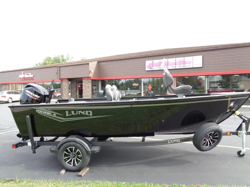 The Image of 2025 Lund 1650 Rebel XL Tiller boat on trailer, parked outside a building. - 0