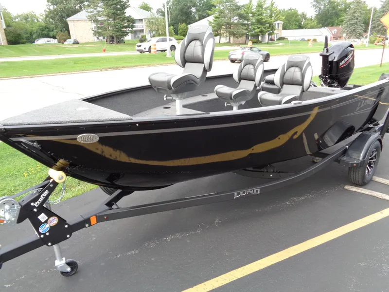 Slide: The Image of 2025 Lund 1650 Rebel XL Tiller boat on trailer, black exterior, parked outdoors. - 3