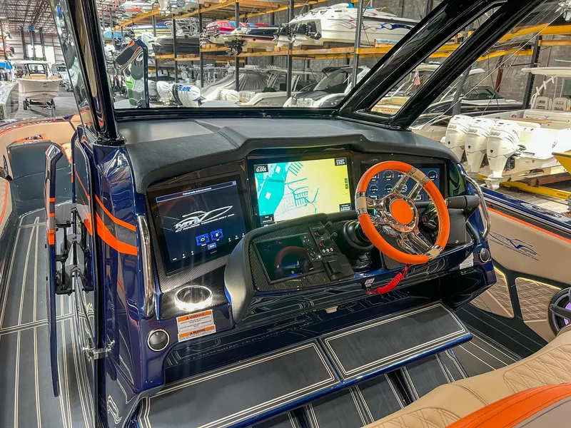 Slide: The Image of 2024 MTI V42 boat dashboard with advanced navigation screens and orange-accented steering wheel. - 12