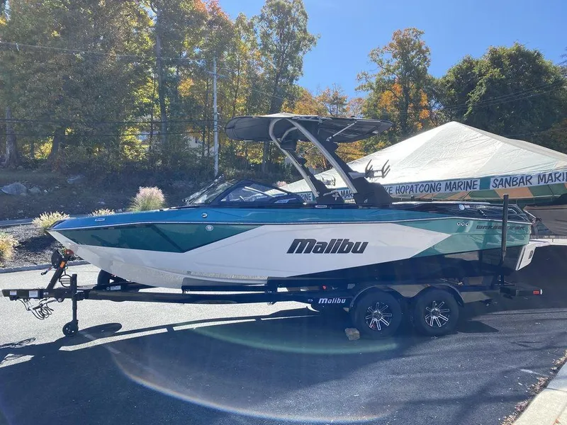 Slide: The Image of 2025 Malibu 23 LSV boat on trailer, parked outdoors with trees in background. - 7