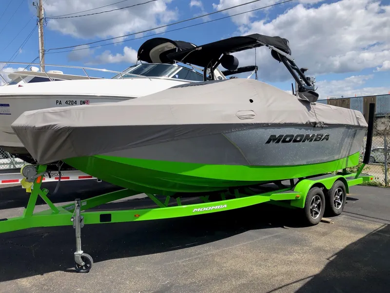 Slide: The Image of 2018 Moomba Max boat with cover on green trailer, parked outdoors. - 2