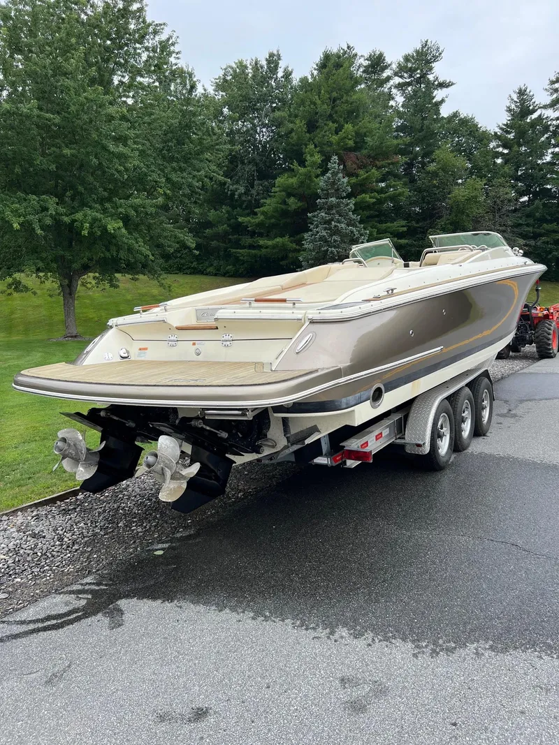 Slide: The Image of 2014 Chris-Craft 32 Launch boat on trailer, parked on a road with trees in the background. - 8