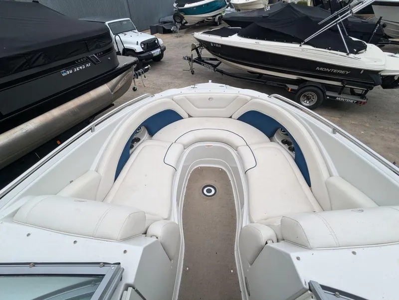 Slide: The Image of 2009 Crownline 240 LS boat interior with white and blue seating, parked among other boats. - 8