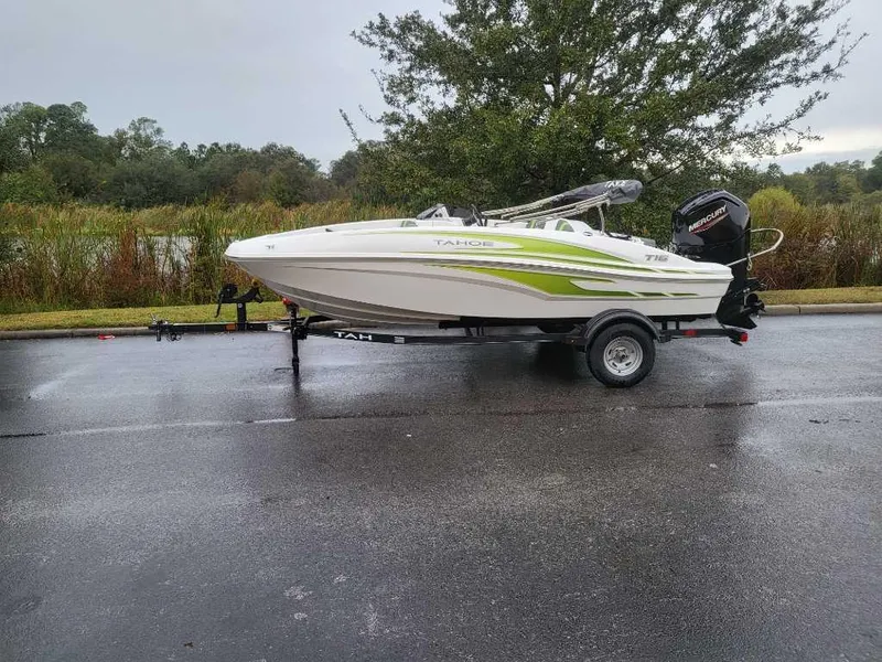 Slide: The Image of 2024 Tahoe T16 boat on trailer, parked on wet pavement near greenery. - 4