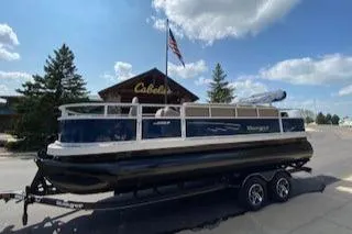 The Image of 2024 Ranger Reata 200F pontoon boat on trailer outside Cabela's store. - 0