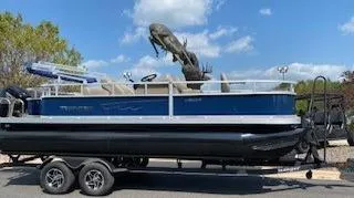 Slide: The Image of 2024 Ranger Reata 200F pontoon boat on trailer, parked outdoors under blue sky. - 3