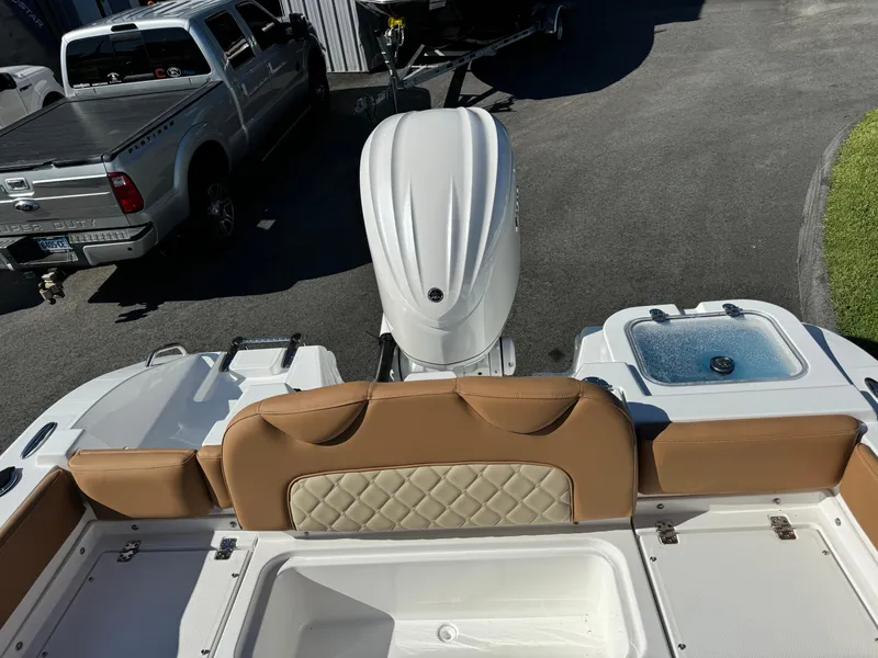 Slide: The Image of 2025 NauticStar 24 OSL boat with tan seating and outboard motor, parked near trucks. - 13