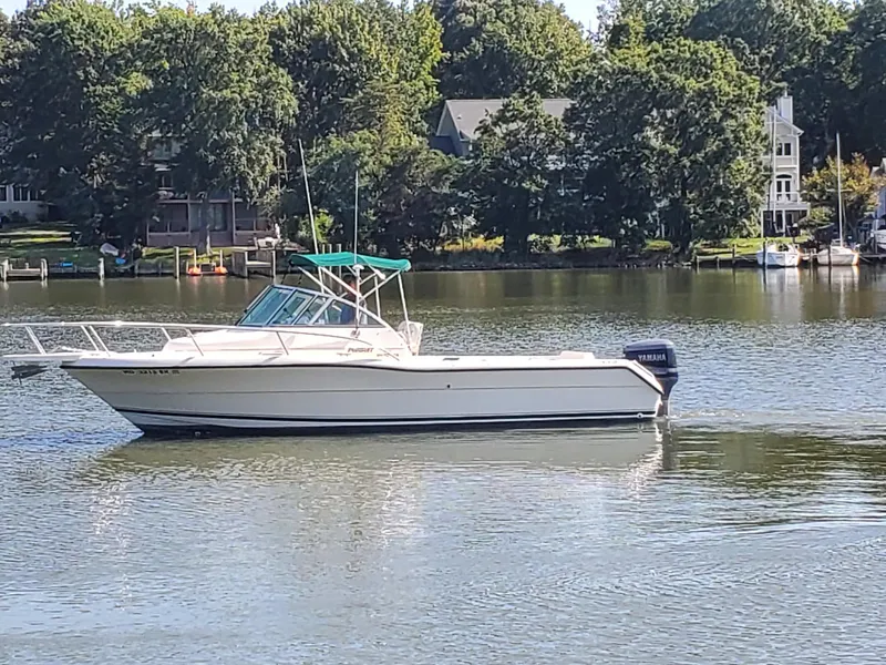 Slide: The Image of 1999 Pursuit 2470 Walkaround boat on a calm lake with trees in the background. - 1