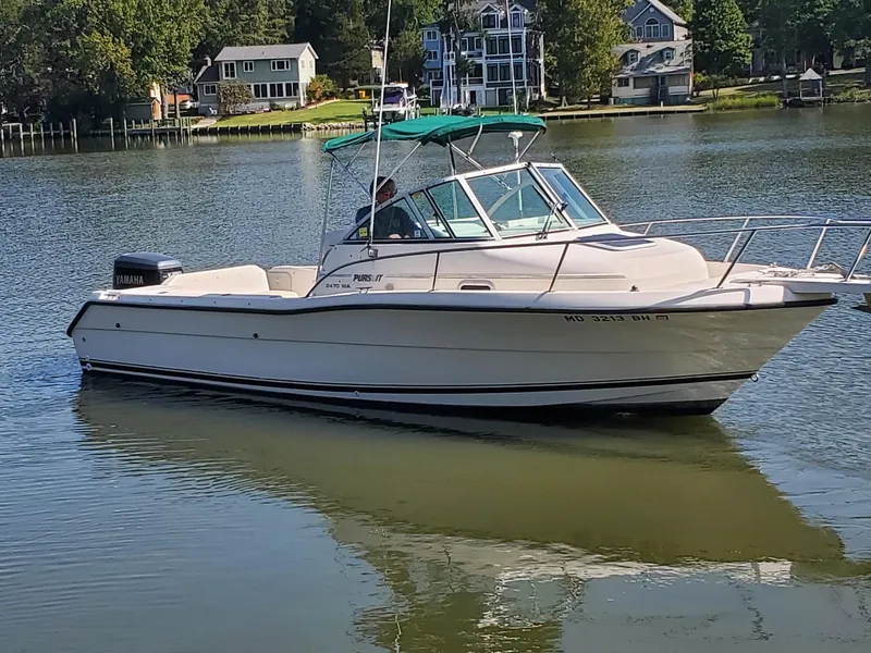 Slide: The Image of 1999 Pursuit 2470 Walkaround boat on calm lake with houses in the background. - 2