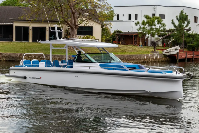 Slide: The Image of 2024 Axopar 37 Sun Top boat cruising on a calm river near residential area. - 23