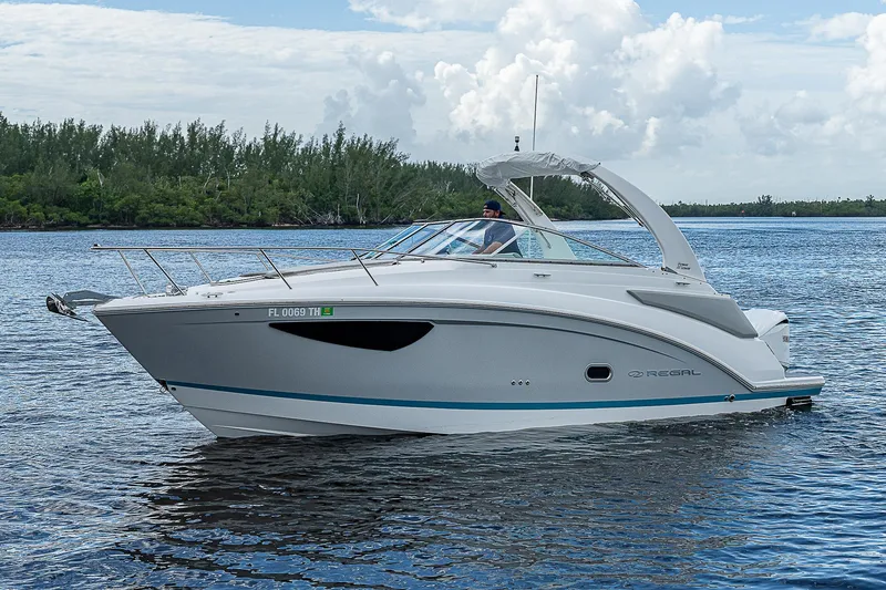 Slide: The Image of 2022 Regal 26 XO boat cruising on a serene lake with lush greenery. - 33
