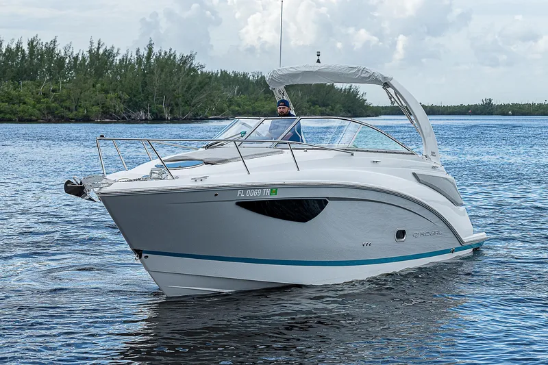 Slide: The Image of 2022 Regal 26 XO boat cruising on a calm lake with lush greenery. - 34
