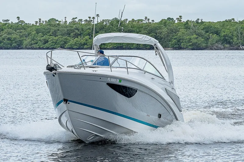 Slide: The Image of 2022 Regal 26 XO boat cruising on a lake with lush greenery in the background. - 46