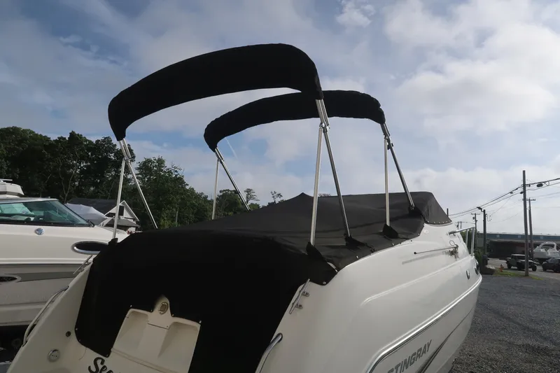 Slide: The Image of 2004 Stingray 240 CS boat with black canopy, parked outdoors under a cloudy sky. - 6
