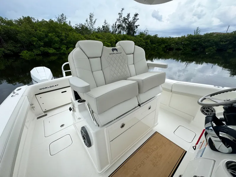 Slide: The Image of 2025 World Cat 280 CC-X boat interior with plush seating and steering wheel, near lush greenery. - 15